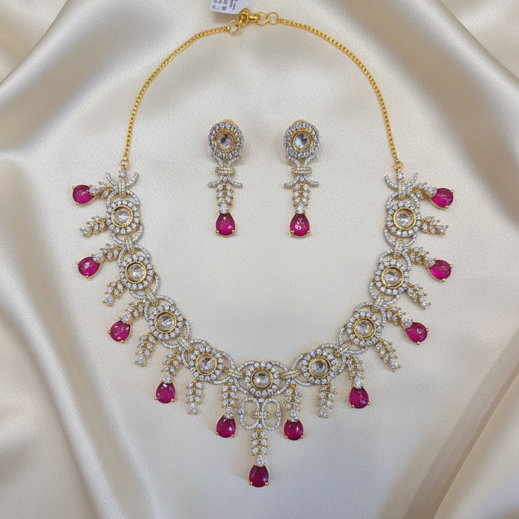 Gold-tone floral necklace set with ruby-colored teardrop drops and matching earrings laid flat on ivory silk
