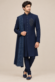 Front three-quarter view of model wearing navy beaded-collar sherwani set with matching churidar and dupatta