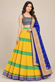 Front-facing model wearing yellow lehenga with horizontal green striped bands, gray patterned blouse and royal-blue drape