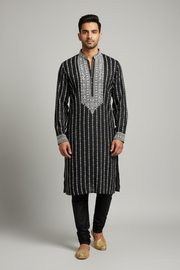 Male model wearing black embroidered kurta set with gold juttis - front pose