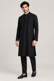 Male model in black shimmer kurta, black trousers and loafers, front three-quarter view