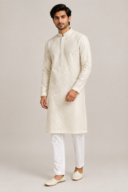 Male model wearing the ivory textured kurta with a stand collar and front placket band, white trousers and juttis, front three-quarter view
