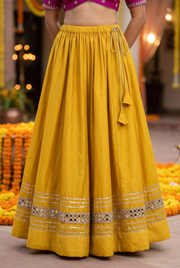 Mustard-yellow skirt on model showing gathered adjustable drawstring waist, tassel ties and mirror-work lower border through the full hem.