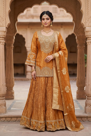 Front view of amber-gold lehenga with embellished long top, pleated skirt and dupatta, styled with jewelry in a traditional courtyard.