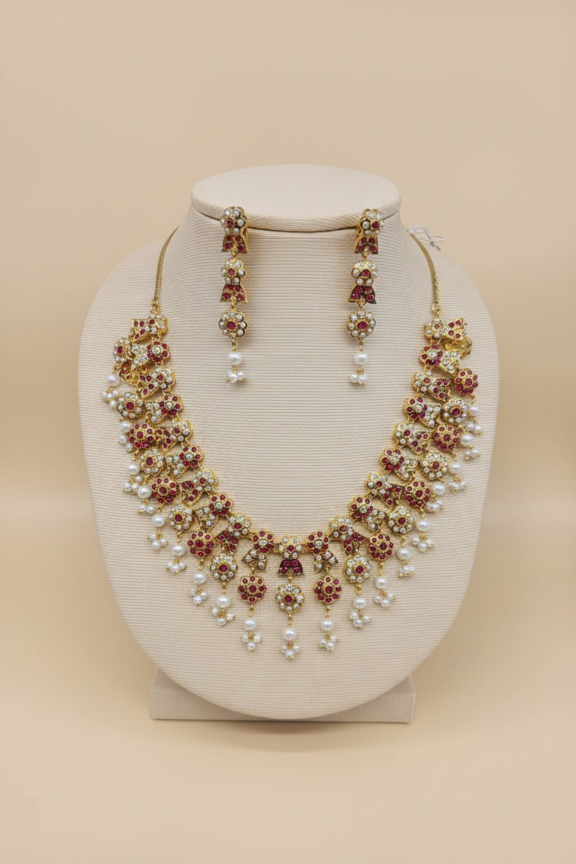 Gold-tone floral necklace set with ruby-colored accents, crystal-style stones, pearl-like drops, and matching earrings on an ivory jewelry bust