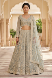 Front view of sage-green and gold-toned lehenga set styled on an adult model in a palace courtyard.