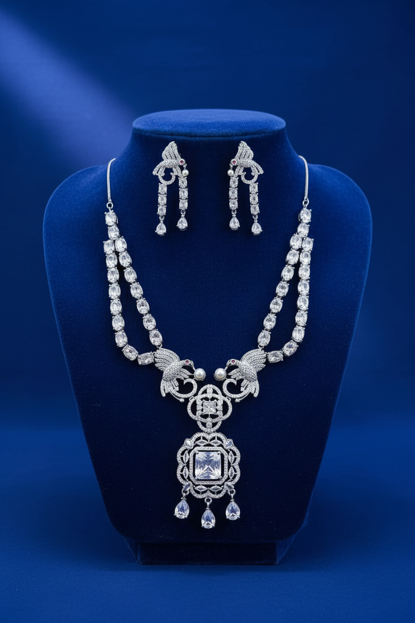 Silver-tone Shristi necklace set with peacock motifs, crystal-style stones, and matching teardrop earrings on royal blue